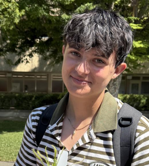 Young person with short dark hair, wearing a striped shirt, smiling and holding a small plant.