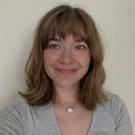 Smiling young woman with shoulder-length light brown hair against a pale wall