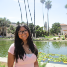 Smiling young woman in glasses by lily pond, palm trees and sunny buildings (photo)